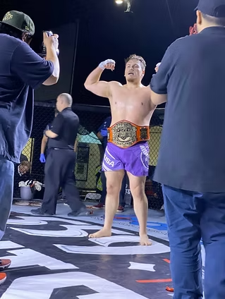 A man in purple shorts is standing on a boxing ring with a belt around his waist.