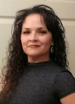 A woman with curly hair is wearing a black shirt and earrings.