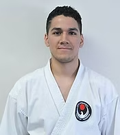 A man in a white karate uniform is standing in front of a white wall.