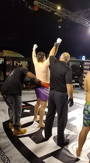 A man is standing in a boxing ring with his arms in the air.