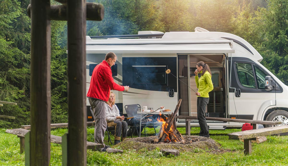 Familj som parkerat husbil och grillar vid en campingplats