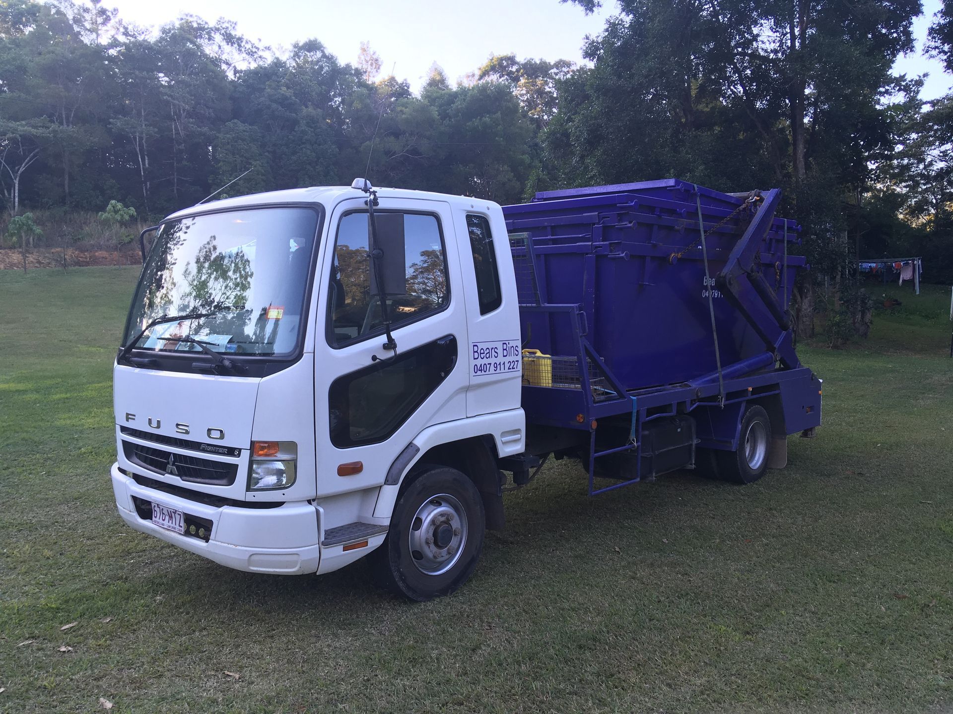 White and blue Fuso truck with a blue container on a grassy field — Bears Bins Skip Hire In Meridan Plains, QLD