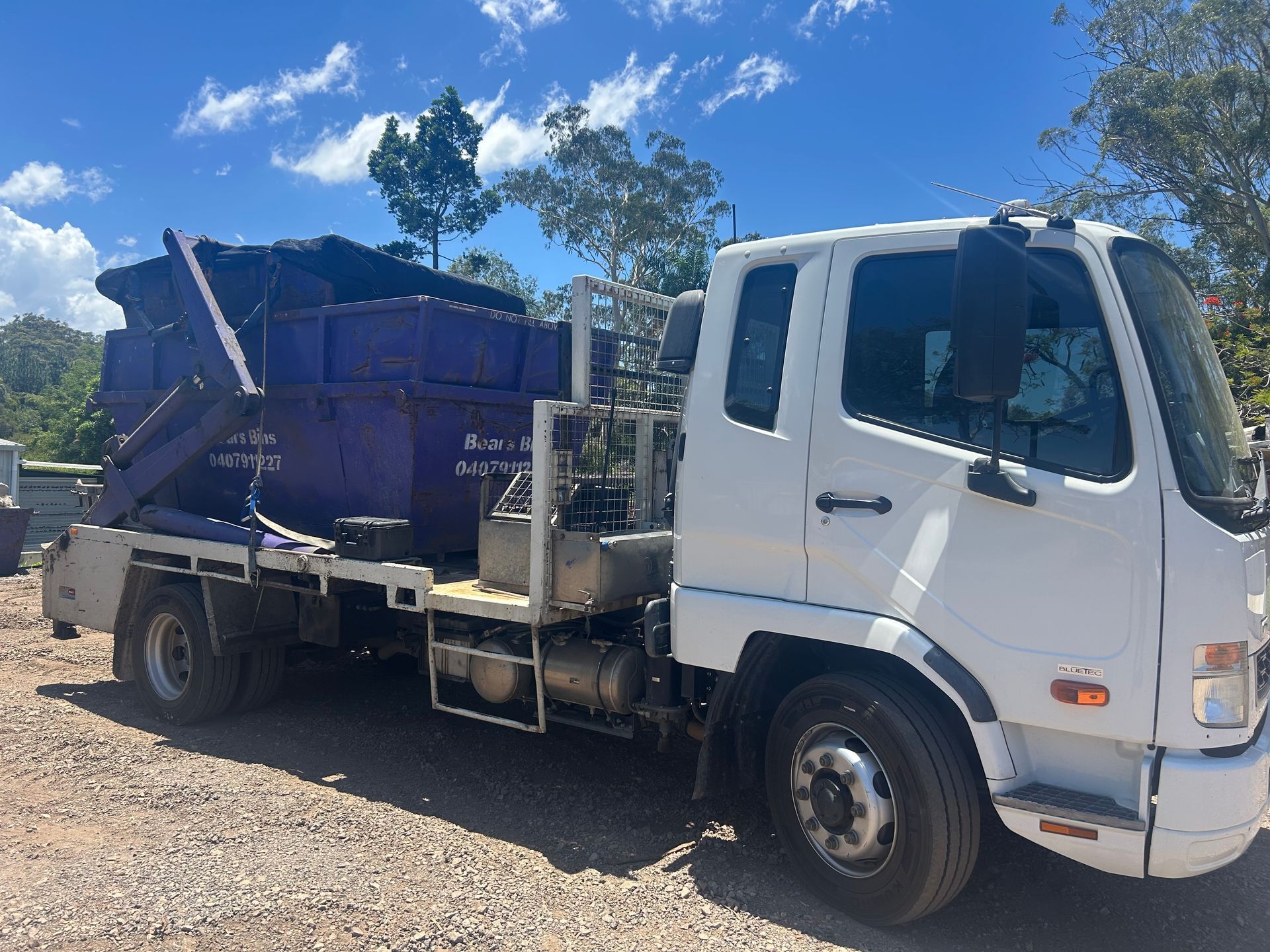 White truck with a purple dumpster on its flatbed, parked outdoors — Bears Bins Skip Hire In Meridan Plains, QLD