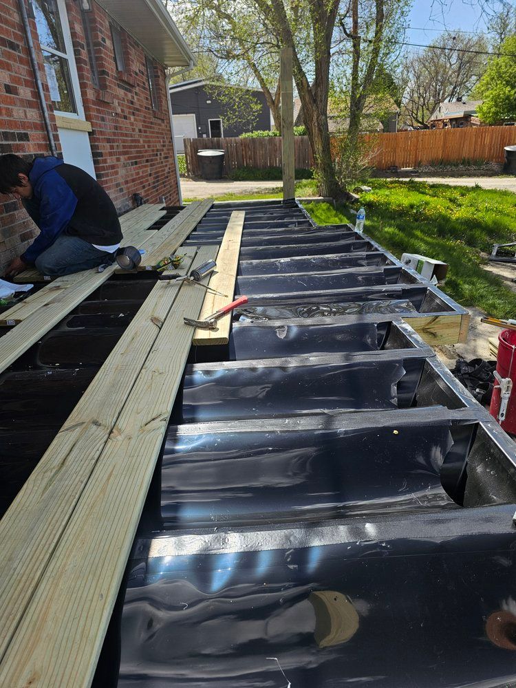 A man is sitting on a wooden deck in front of a brick house.