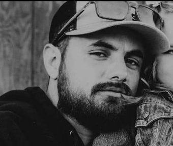 A black and white photo of a man with a beard wearing a hat and sunglasses.