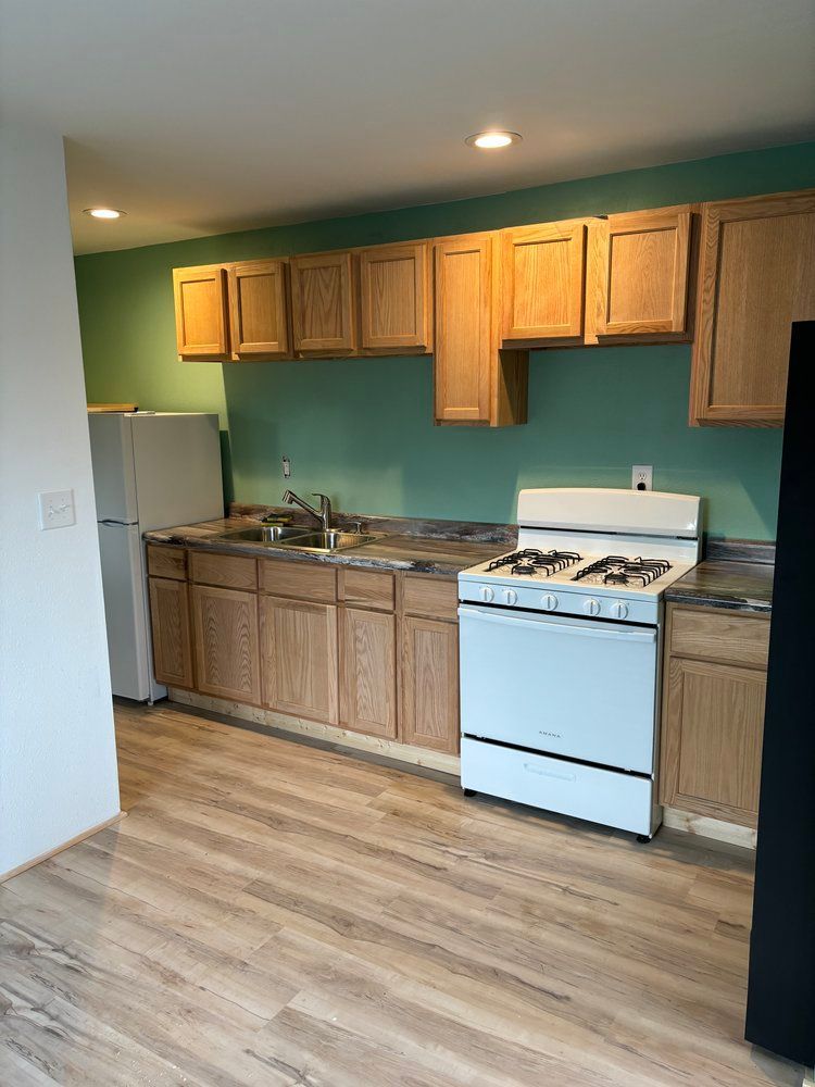 A kitchen with wooden cabinets , a stove , a refrigerator , and a sink.