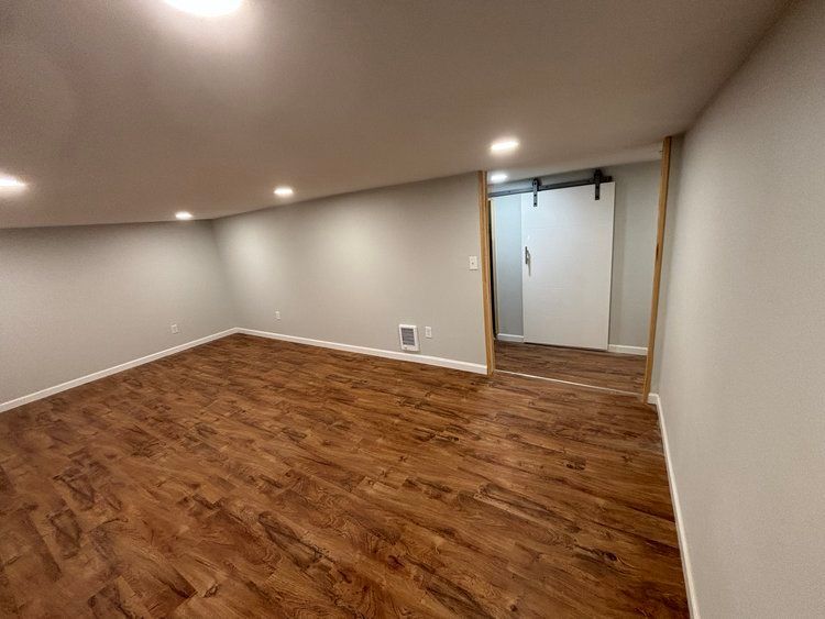 An empty basement with hardwood floors and a sliding barn door.