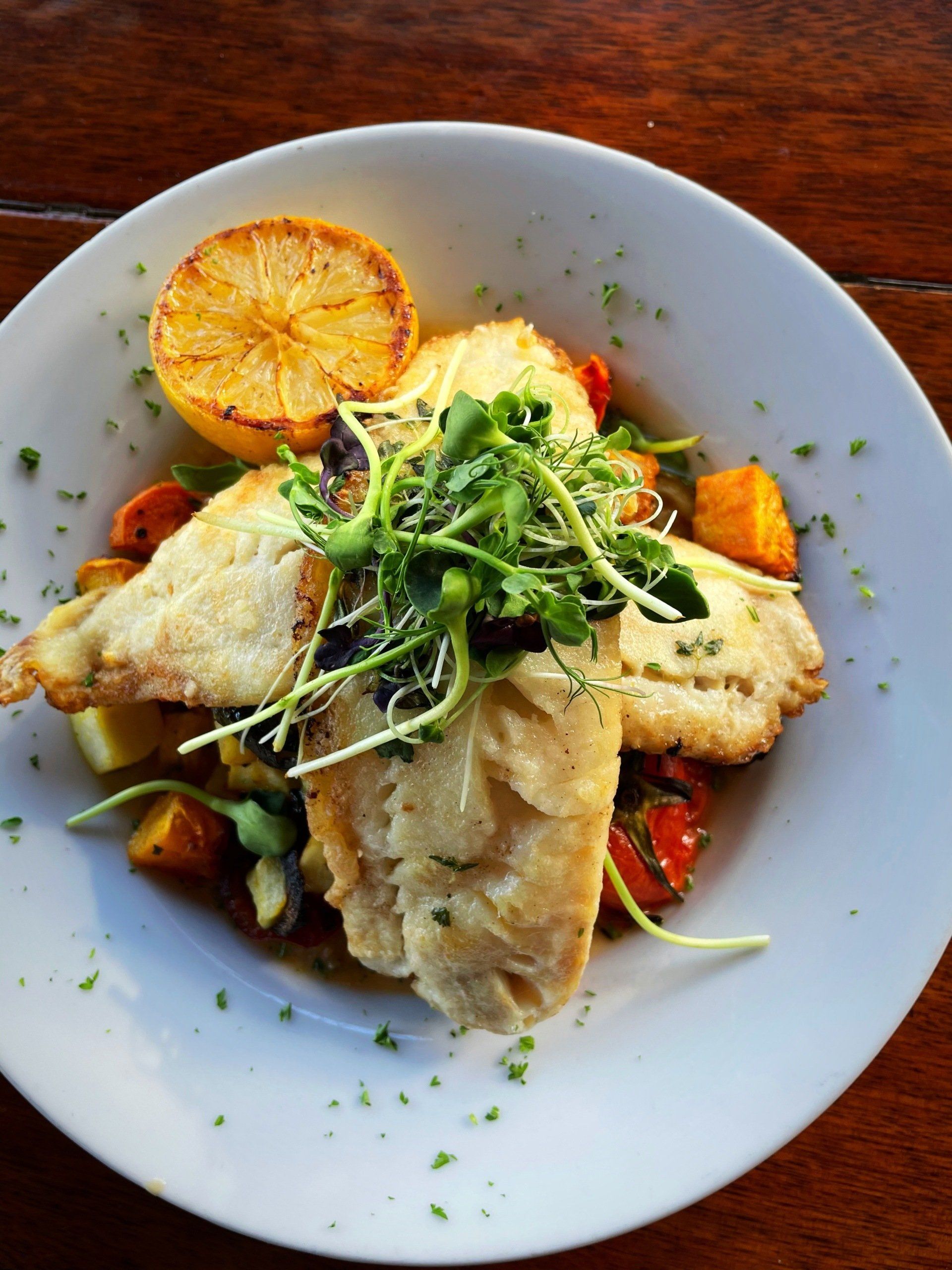 A white plate topped with fish and vegetables on a wooden table