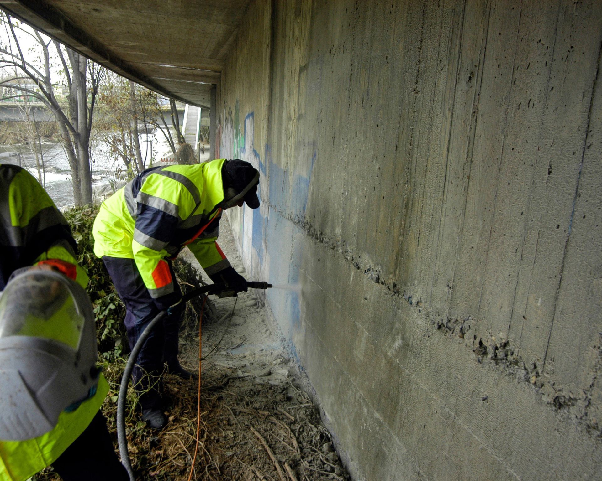 A man in a yellow jacket is working on a concrete wall.