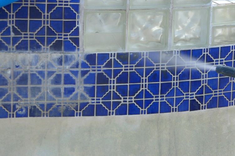 A person is cleaning a blue tile wall with a high pressure washer.