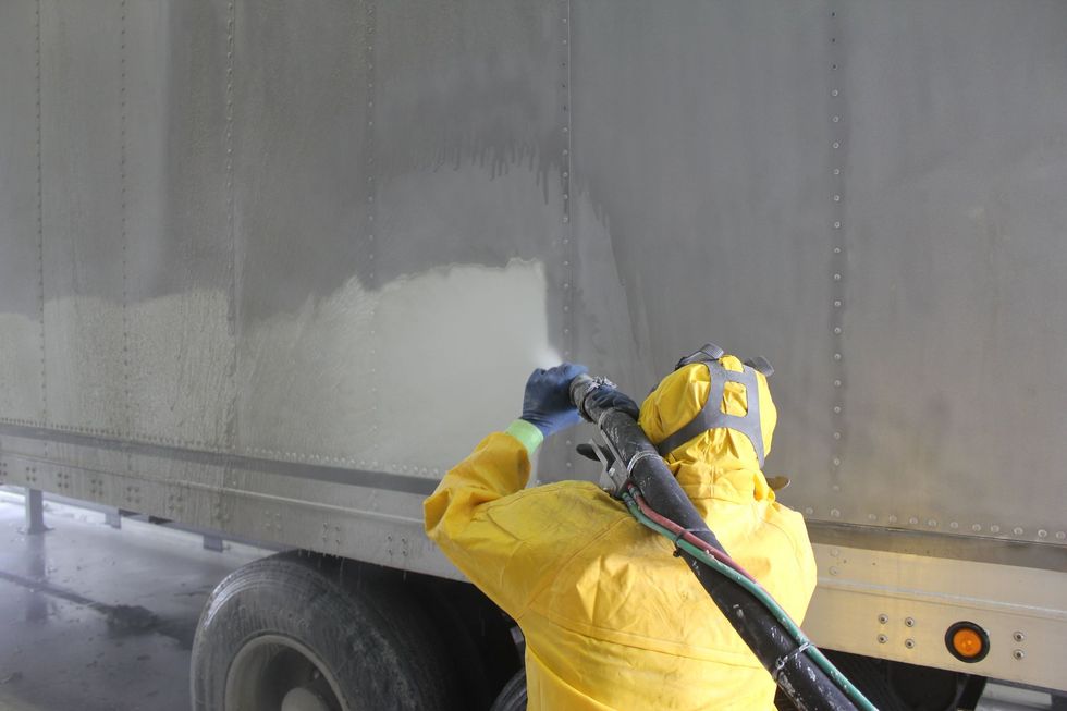 A man in a yellow suit is cleaning the side of a truck.