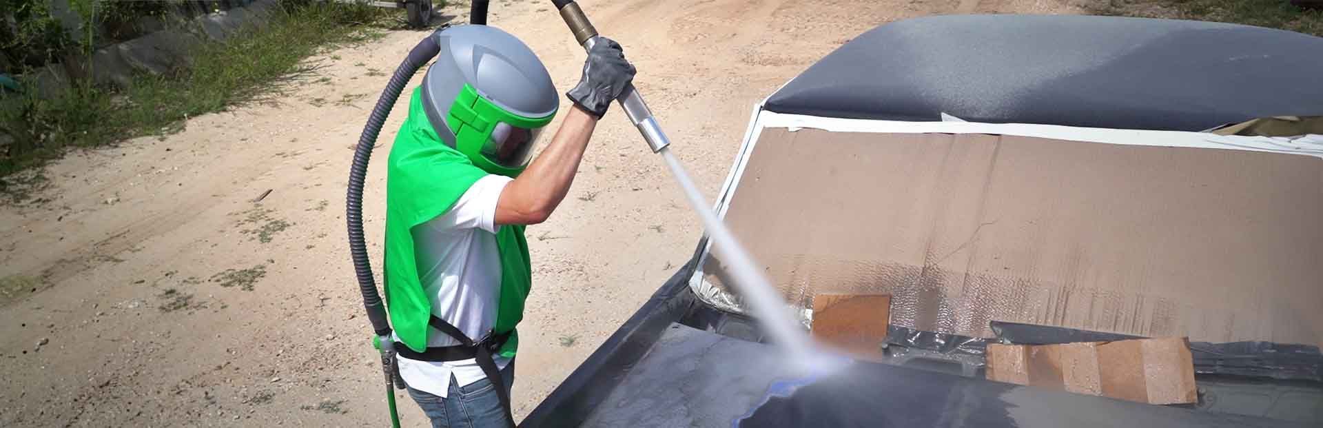 A man is sandblasting a car with a machine.