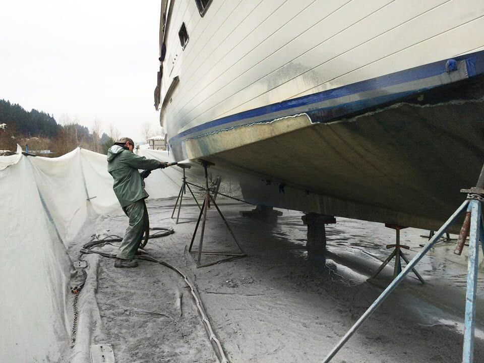 A man is spraying paint on the side of a boat