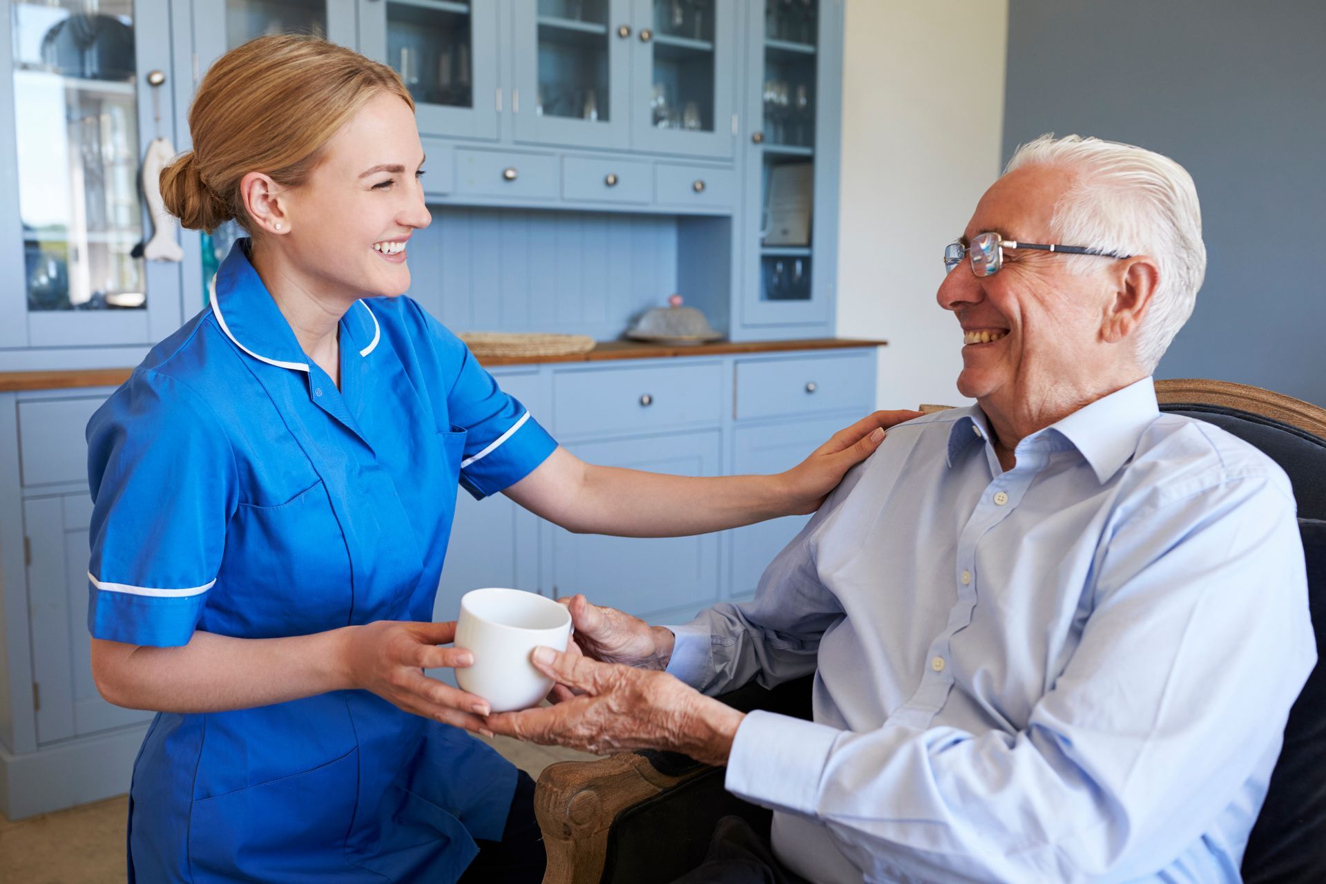 A female carer is chatting and laughing with an elderly male in his porch during her visit.