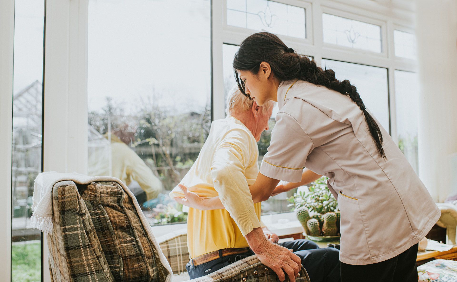 A caregiver is helping an elderly man to sit.