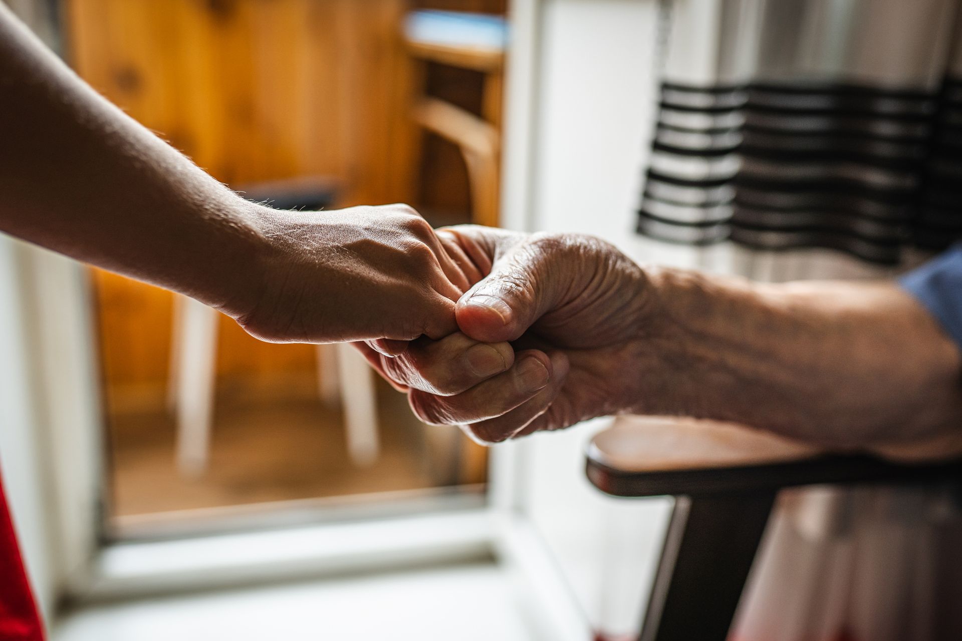 Close-up of a caregiver holding hands with an elderly person.