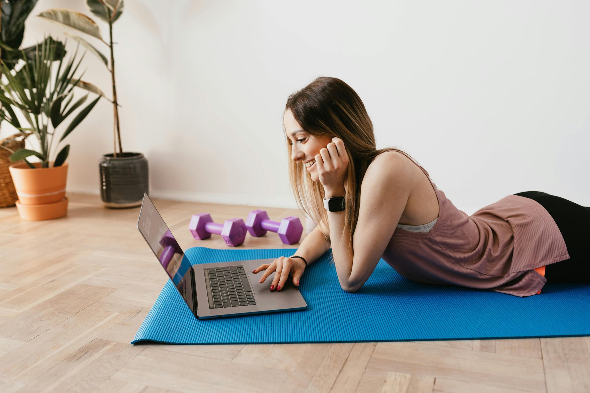 A woman is laying on a yoga mat using a laptop computer.