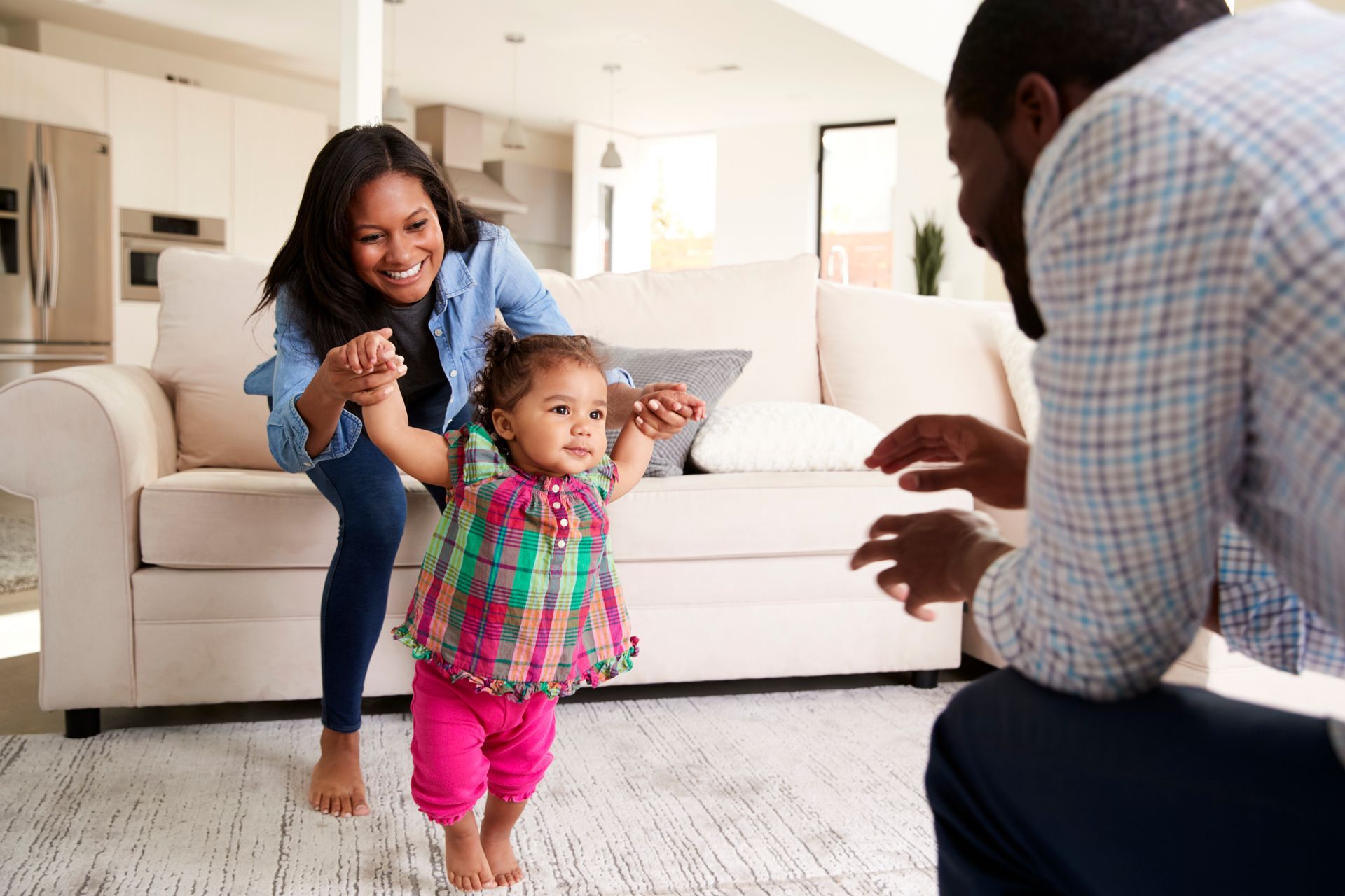man and his wife playing with their toddler daughter, encouraging her to walk