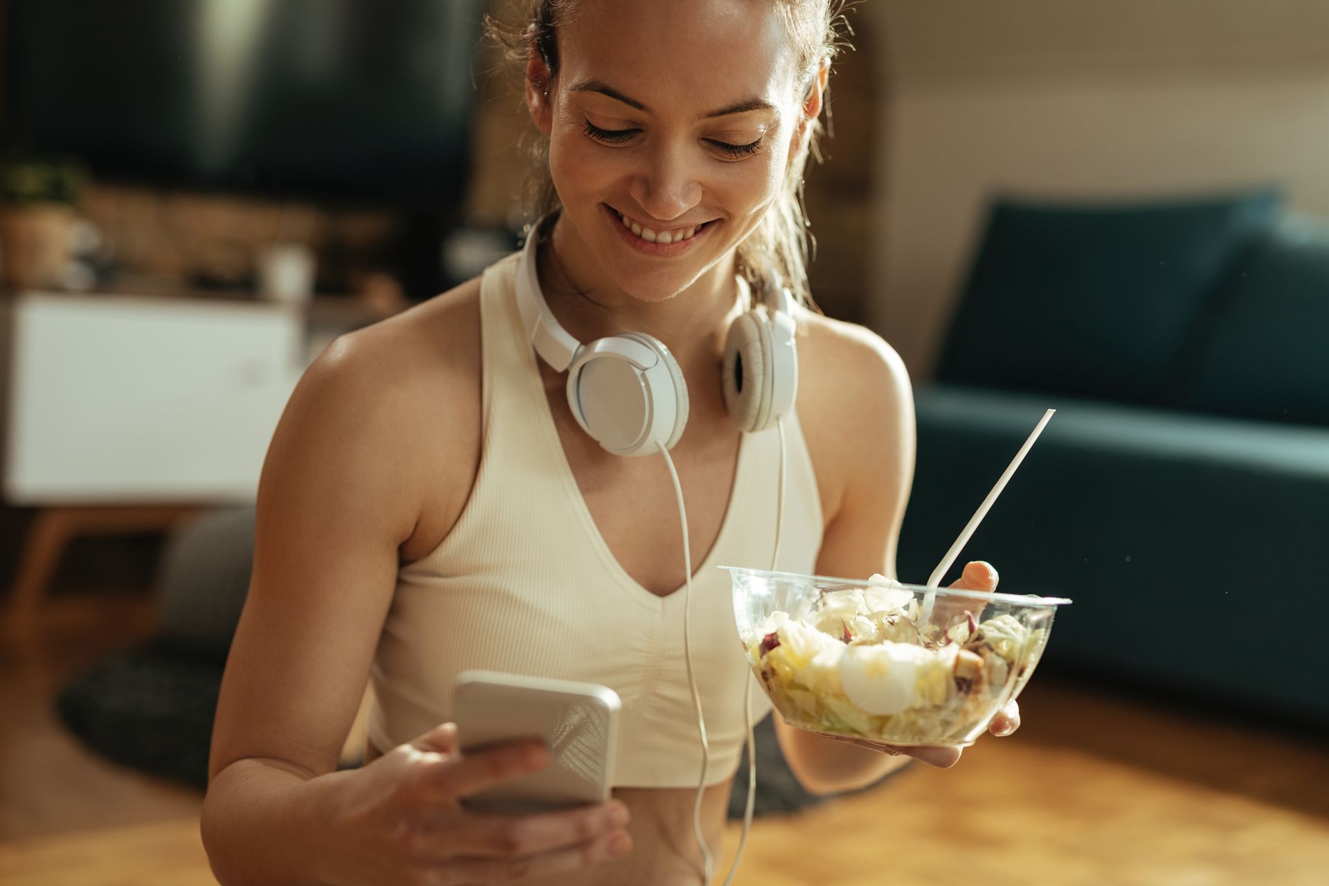 A woman is eating a salad and looking at her phone reviewing her nutrition plan