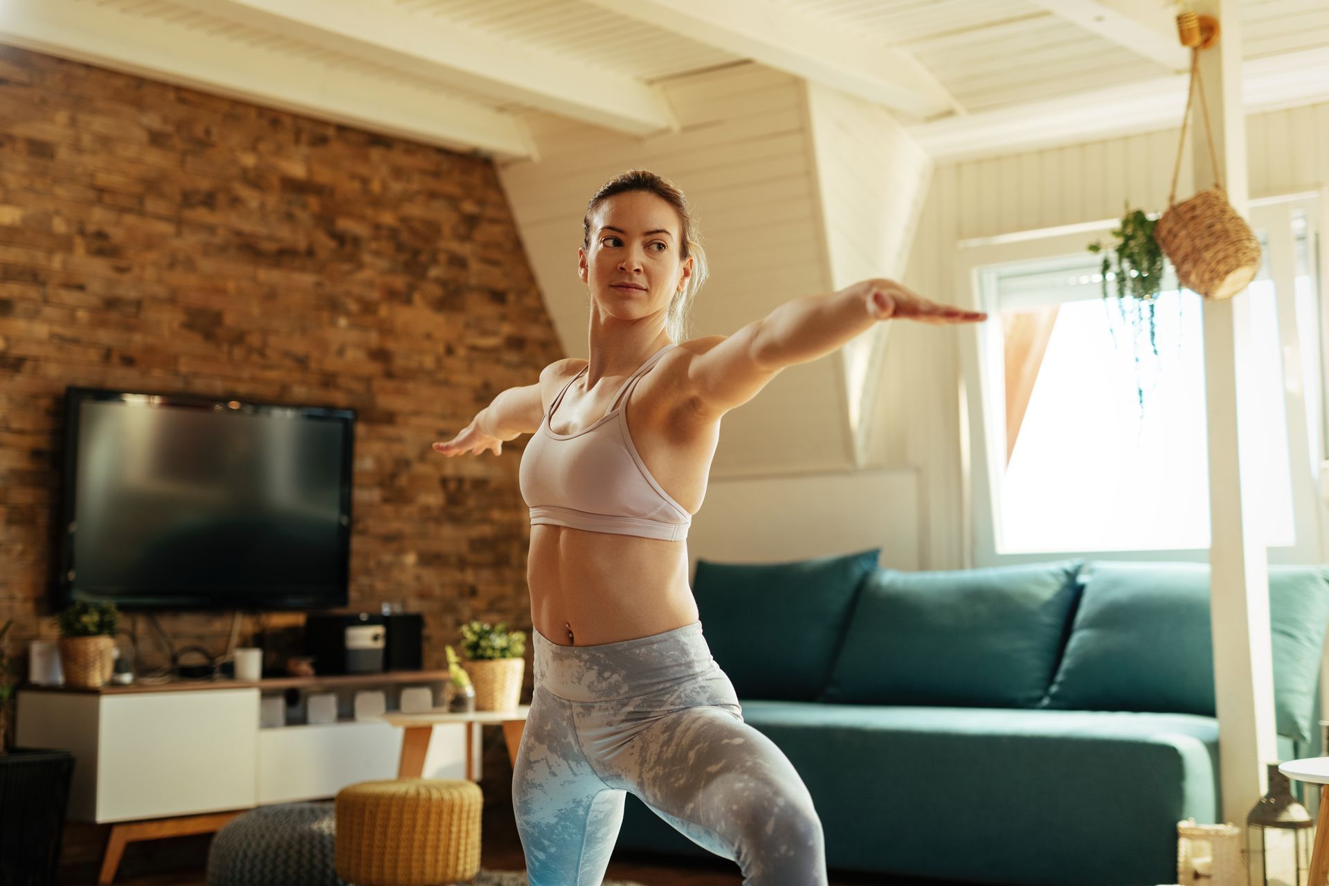 A woman is practicing yoga, warrior ii pose, in a living room.