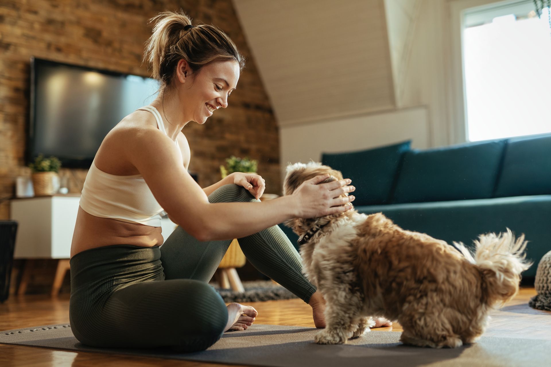 A woman is sitting on a yoga mat with her dog.