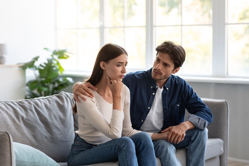 A man is comforting a woman who is sitting on a couch.