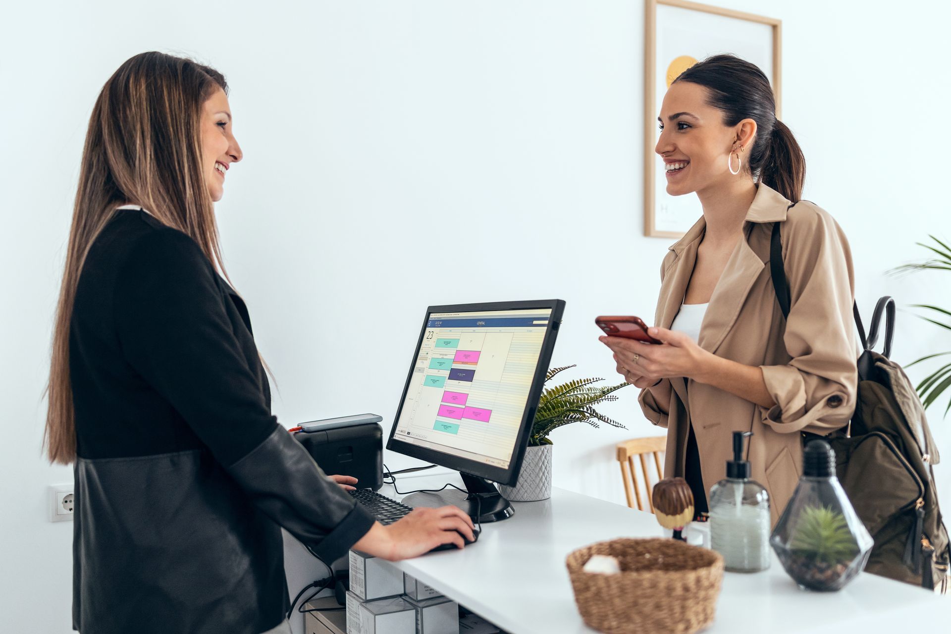 Two women are standing in front of a computer talking to each other.