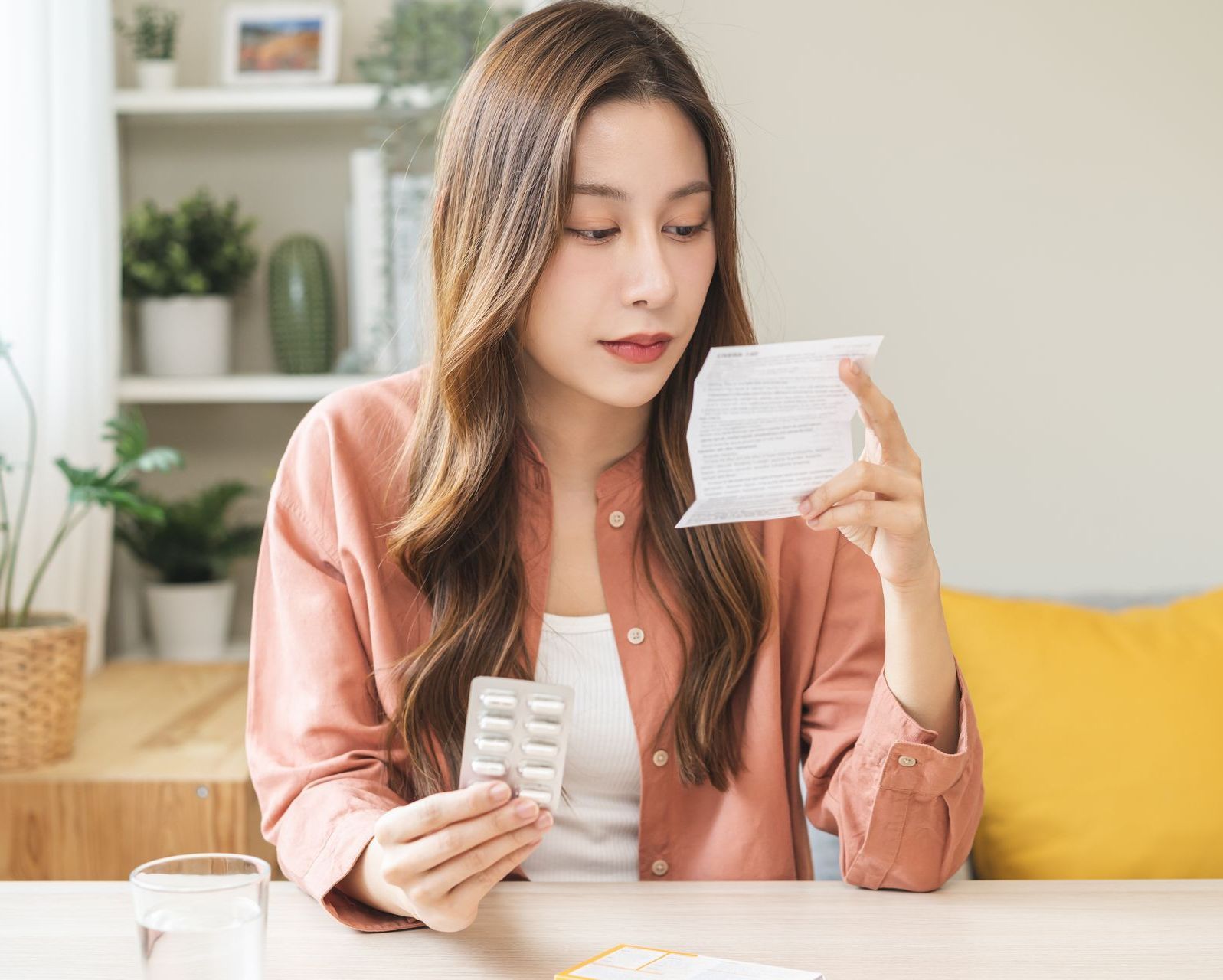 A woman is sitting at a table holding a pack of vitamin C and reading about its effects on fertility.