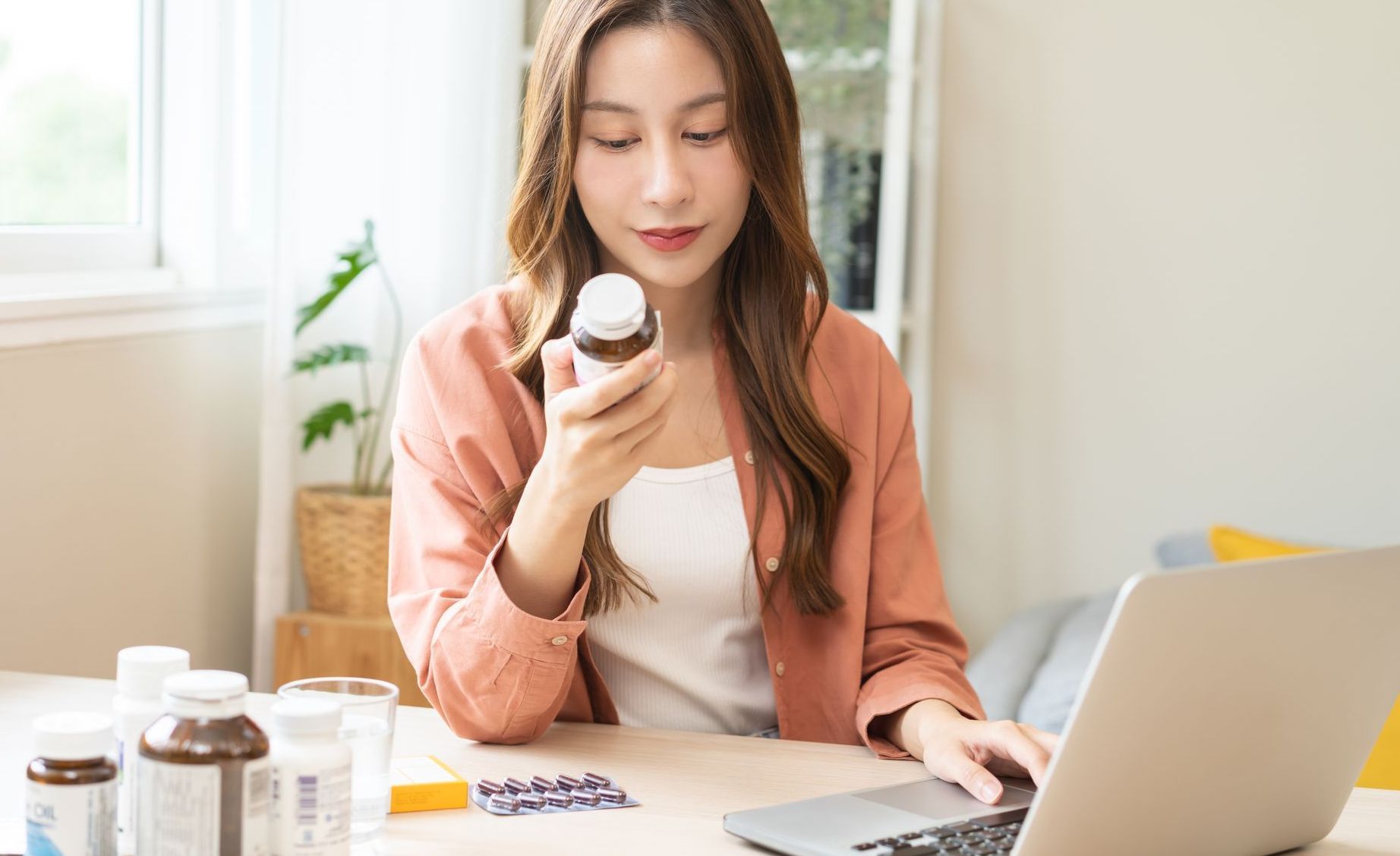 A woman is holding a bottle of supplements while using a laptop computer to research supplements for fertility