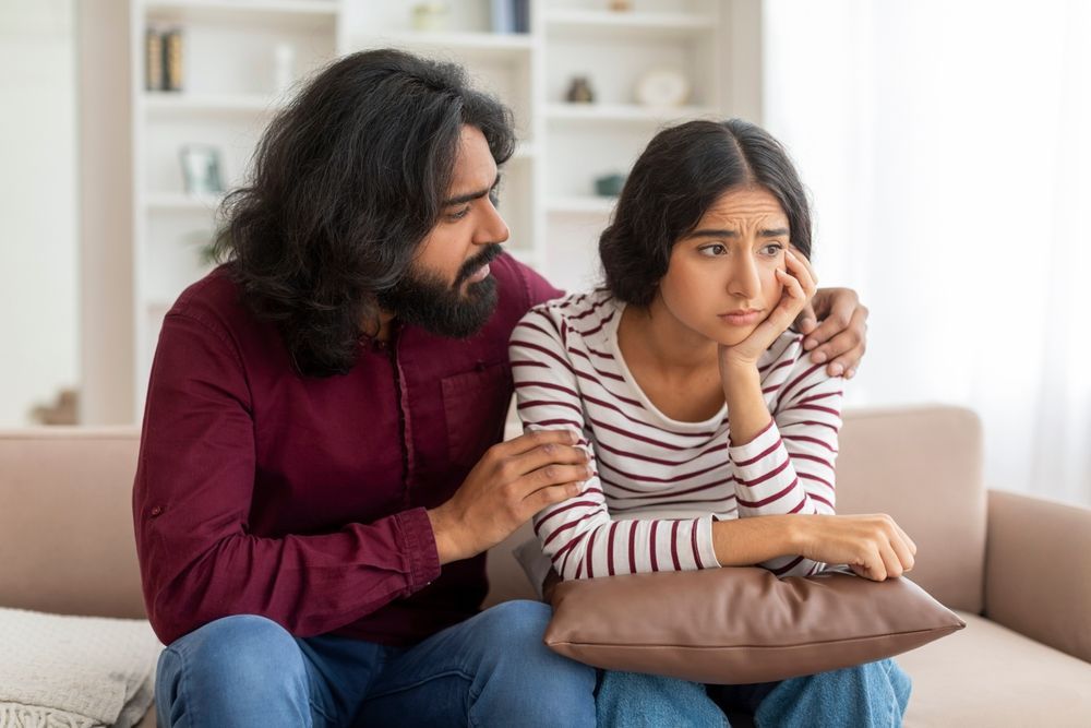 A man is comforting a woman who is sitting on a couch.