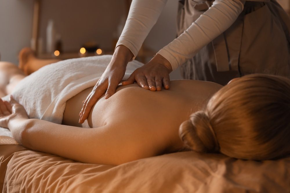 A person receives a massage on their back in a dimly lit, warm-toned spa setting.