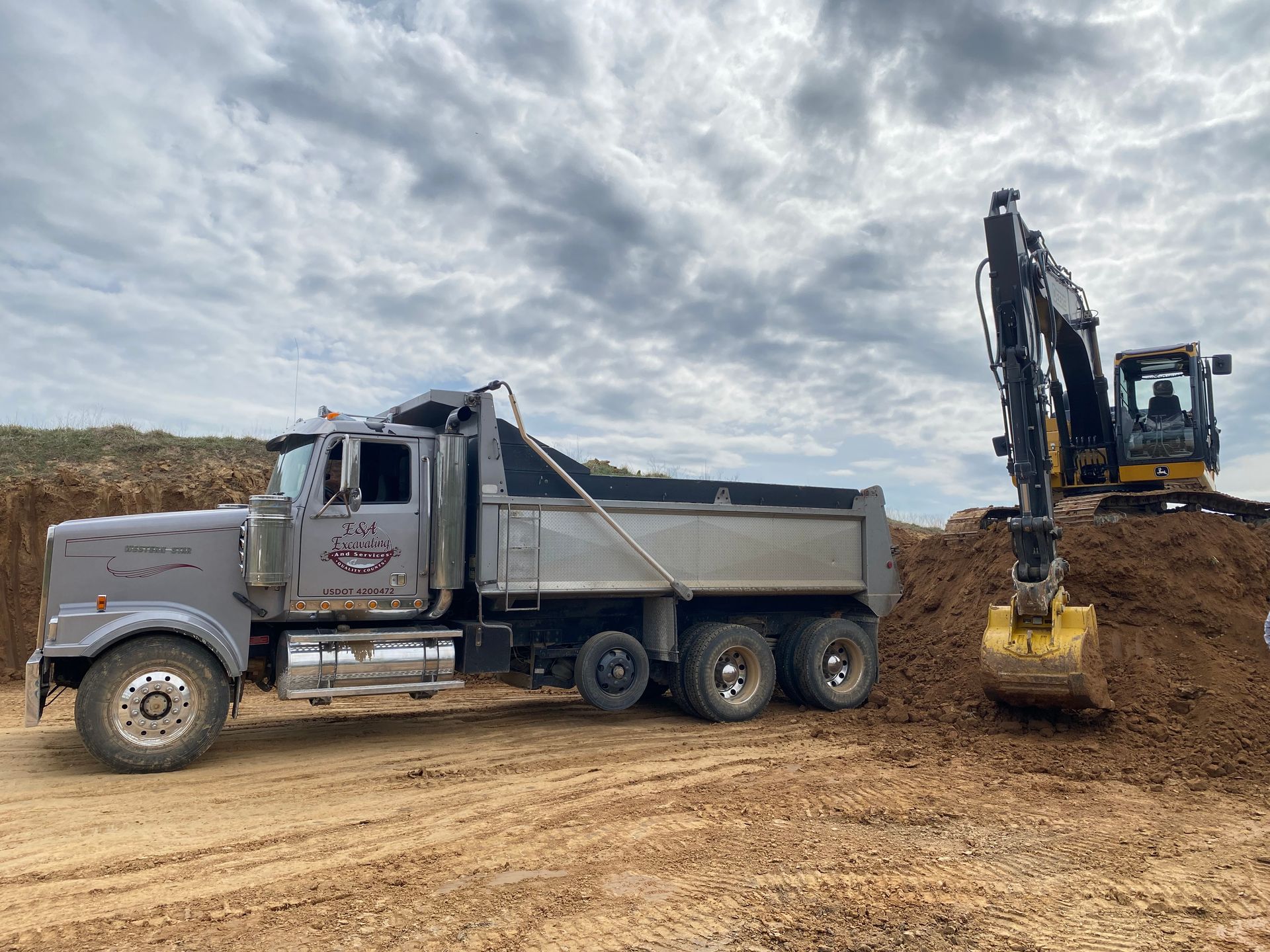 A dump truck is parked next to an excavator in a dirt field.