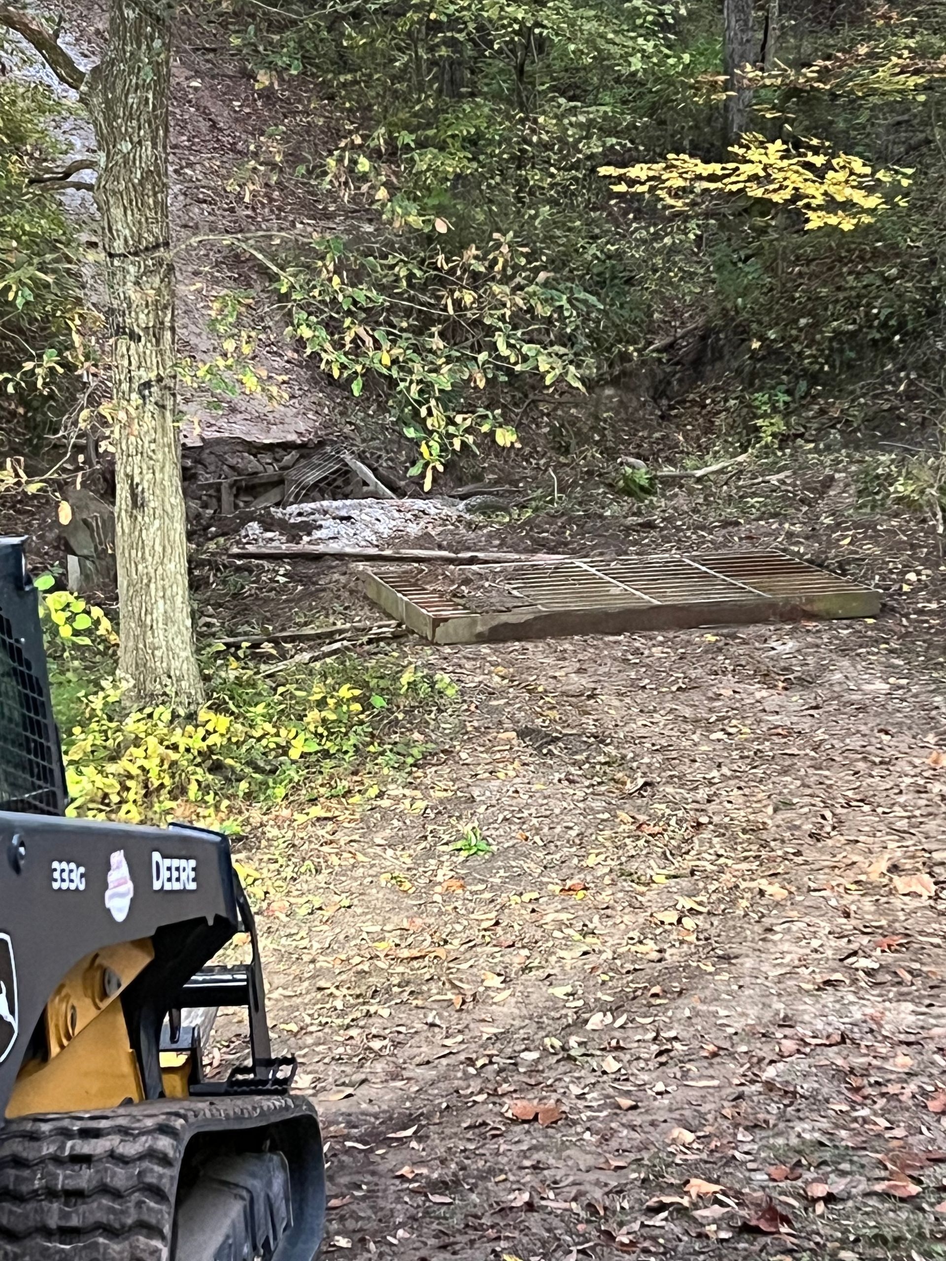 A small tractor is driving down a dirt road in the woods.