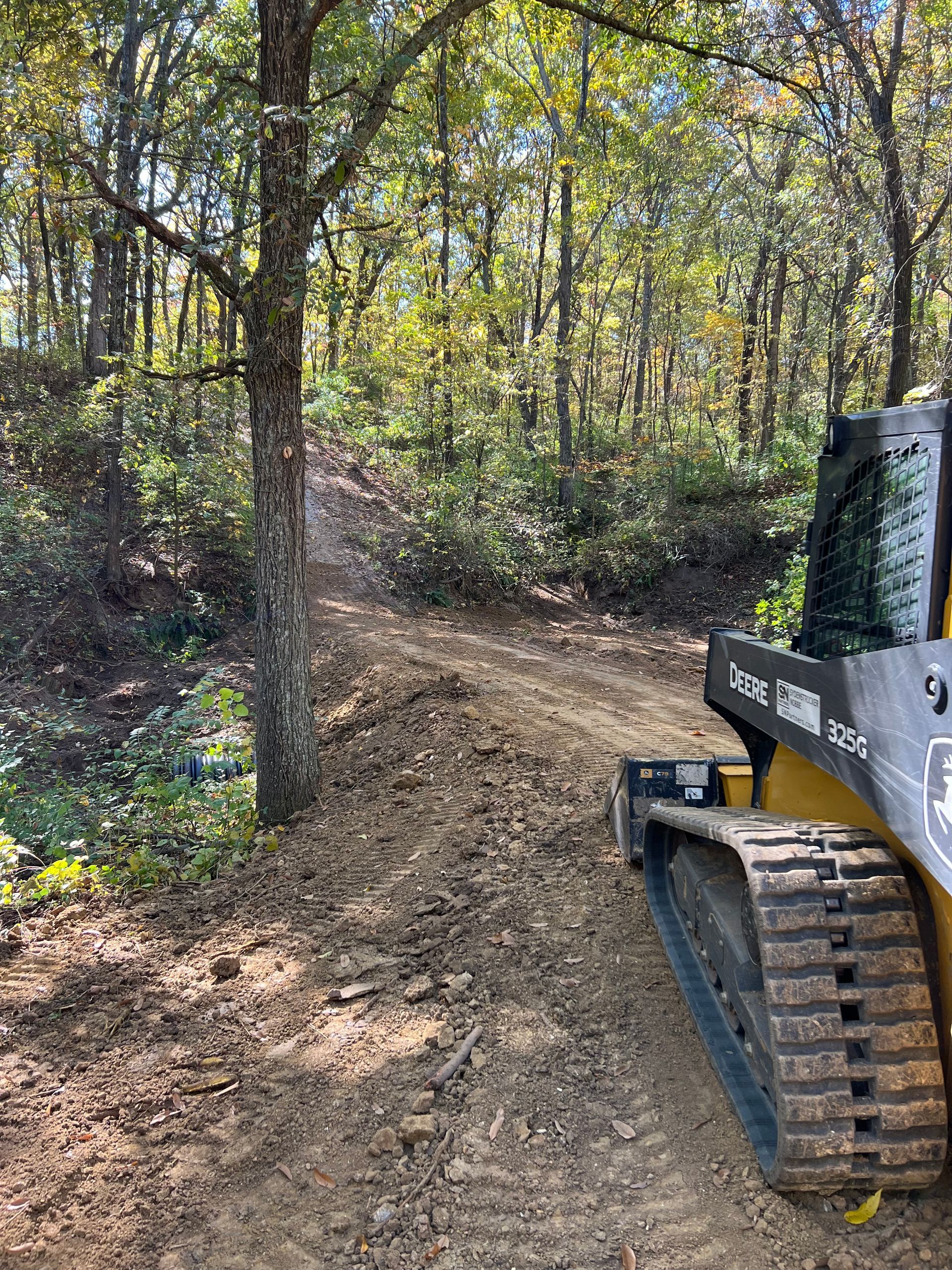 A bulldozer is driving down a dirt road in the woods.