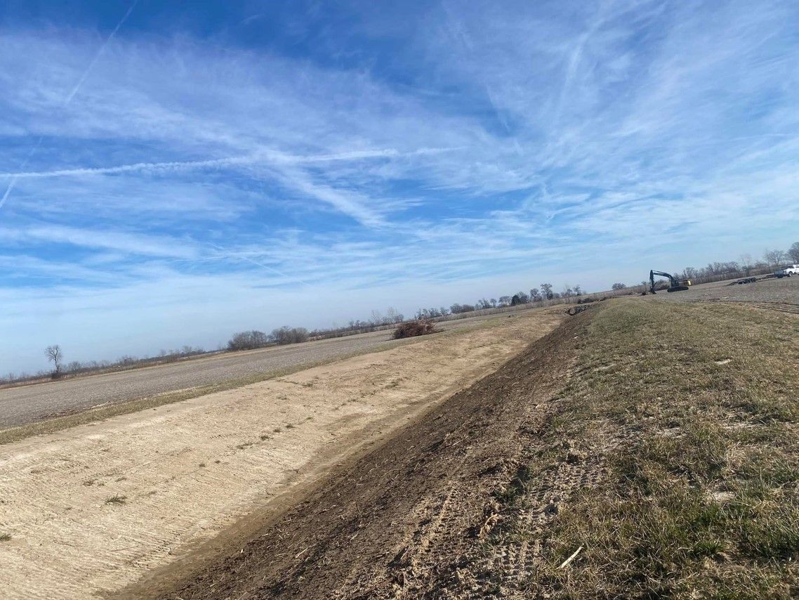 A dirt road going through a field with a blue sky in the background.