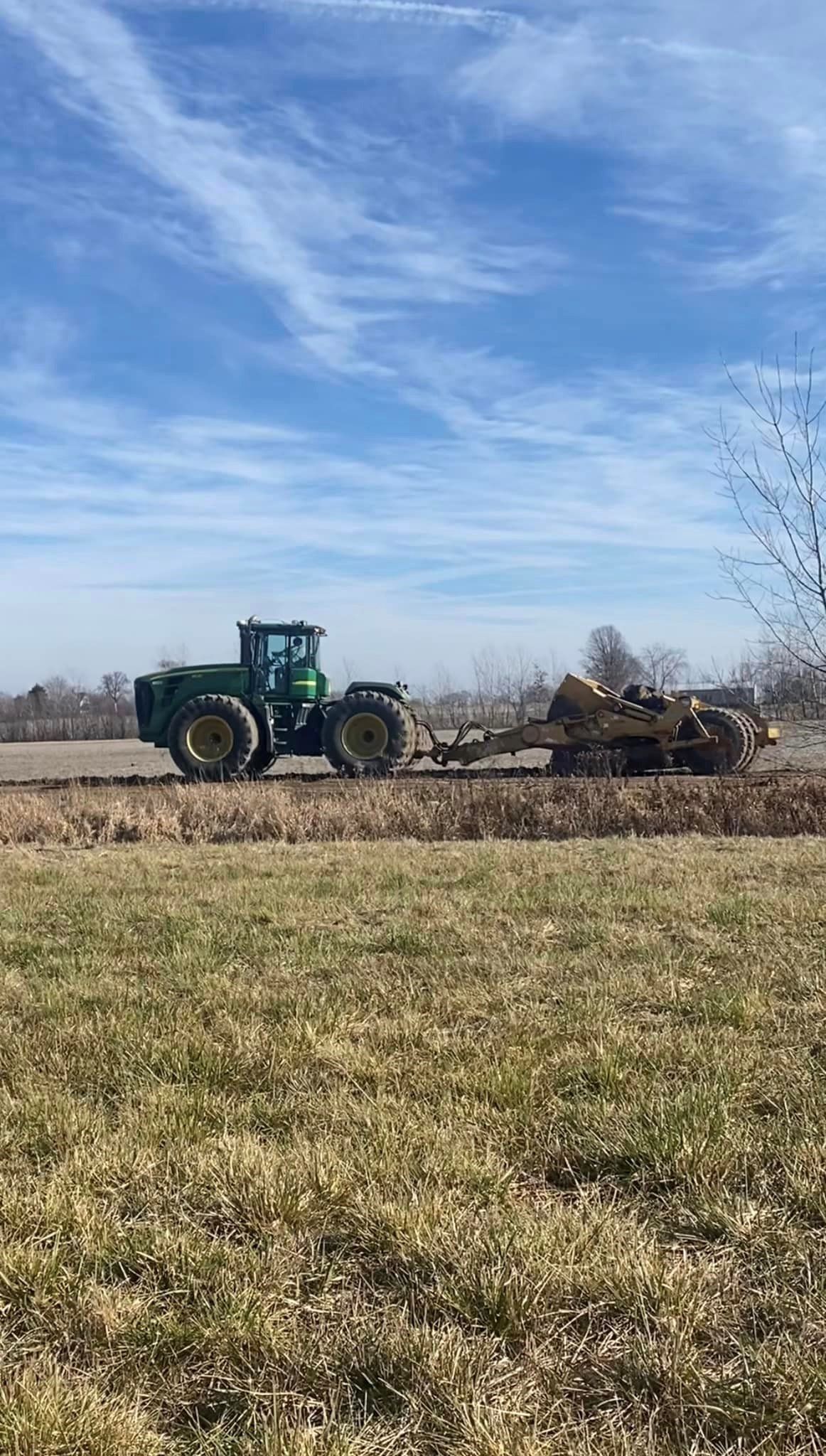 A green tractor is driving through a grassy field.