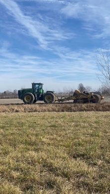 A green tractor is driving through a grassy field.