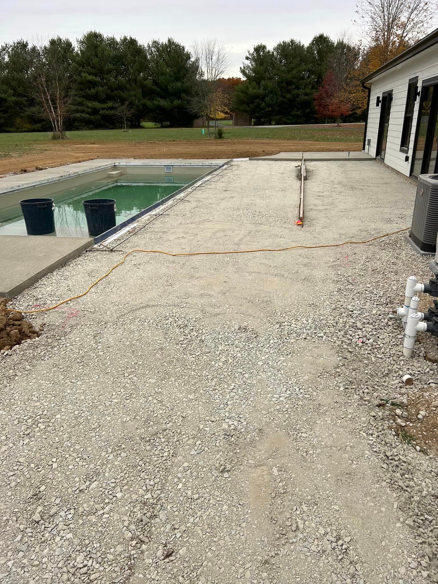 A gravel driveway leading to a swimming pool with a house in the background.