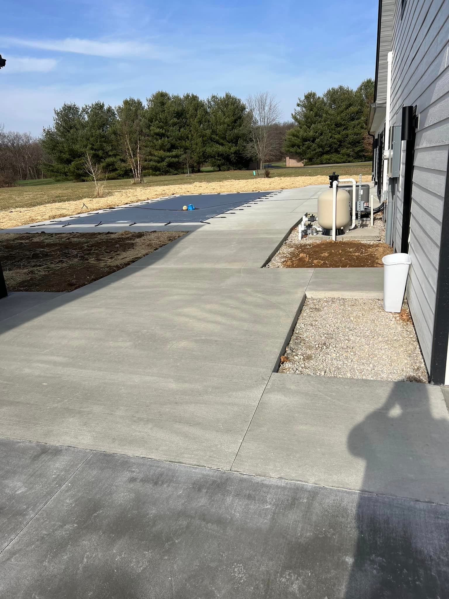 A concrete walkway leading to a house with trees in the background.