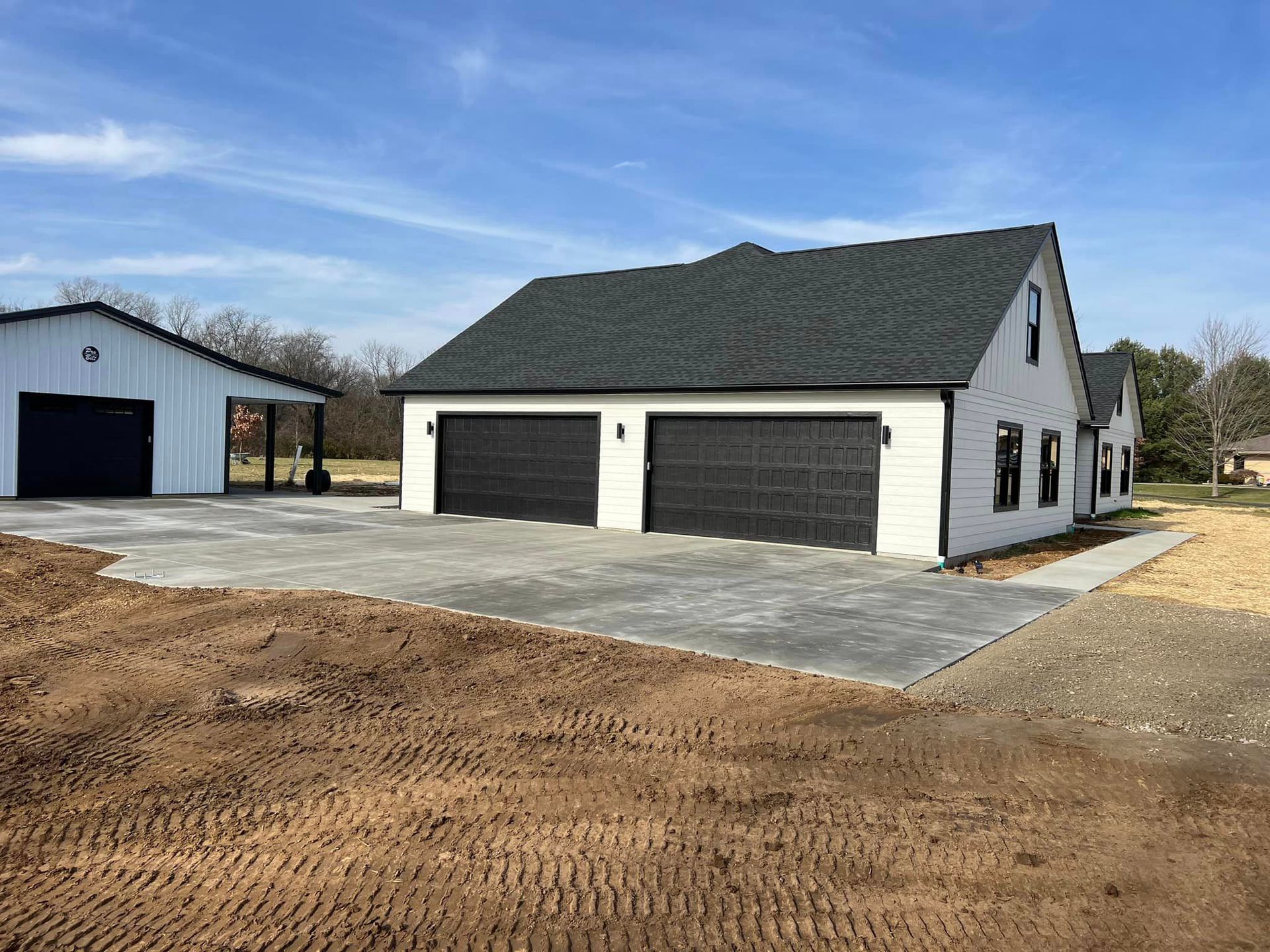 A white house with black garage doors is sitting on top of a dirt field.
