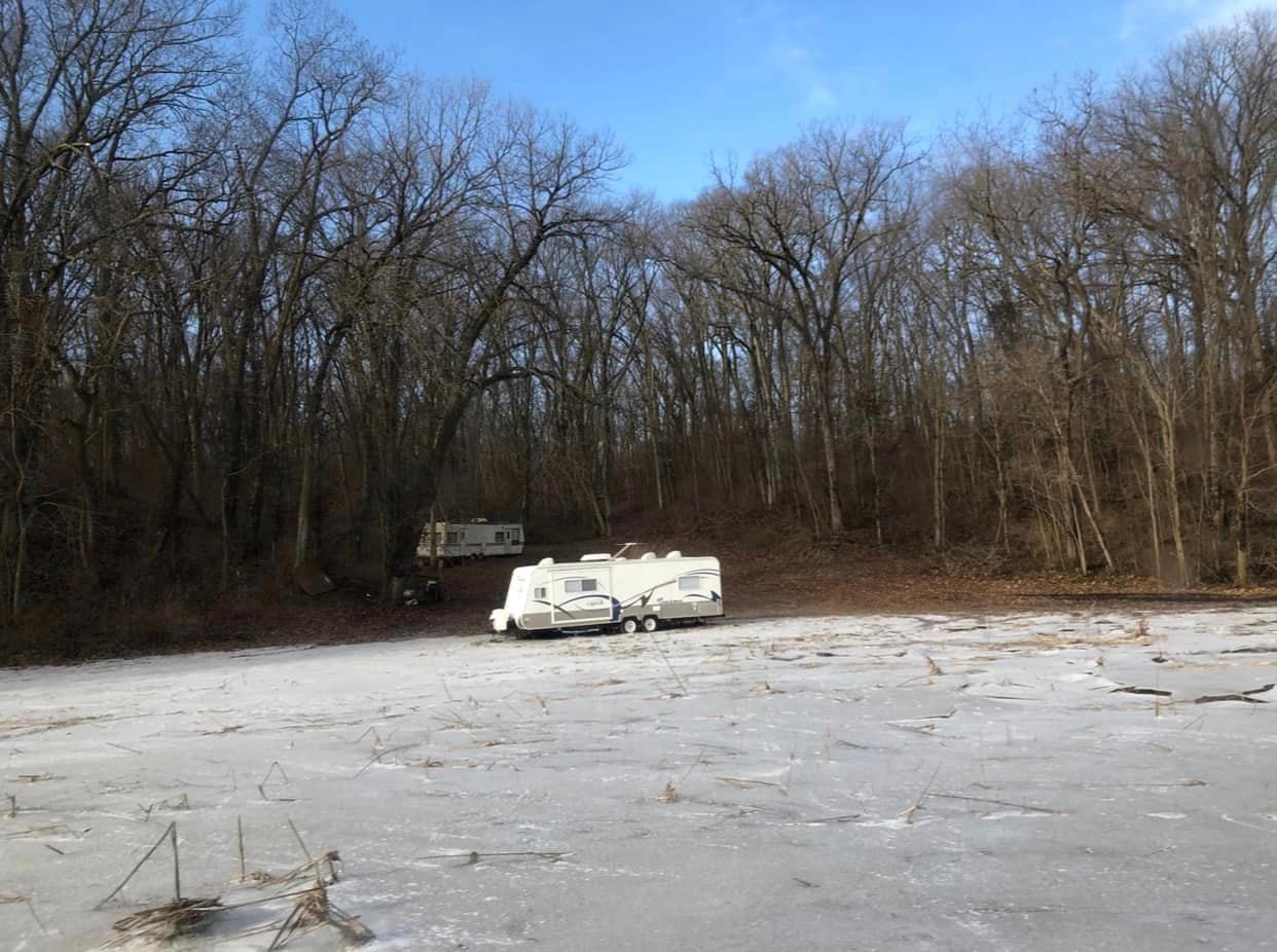 Two rvs are parked on a frozen lake in the woods.