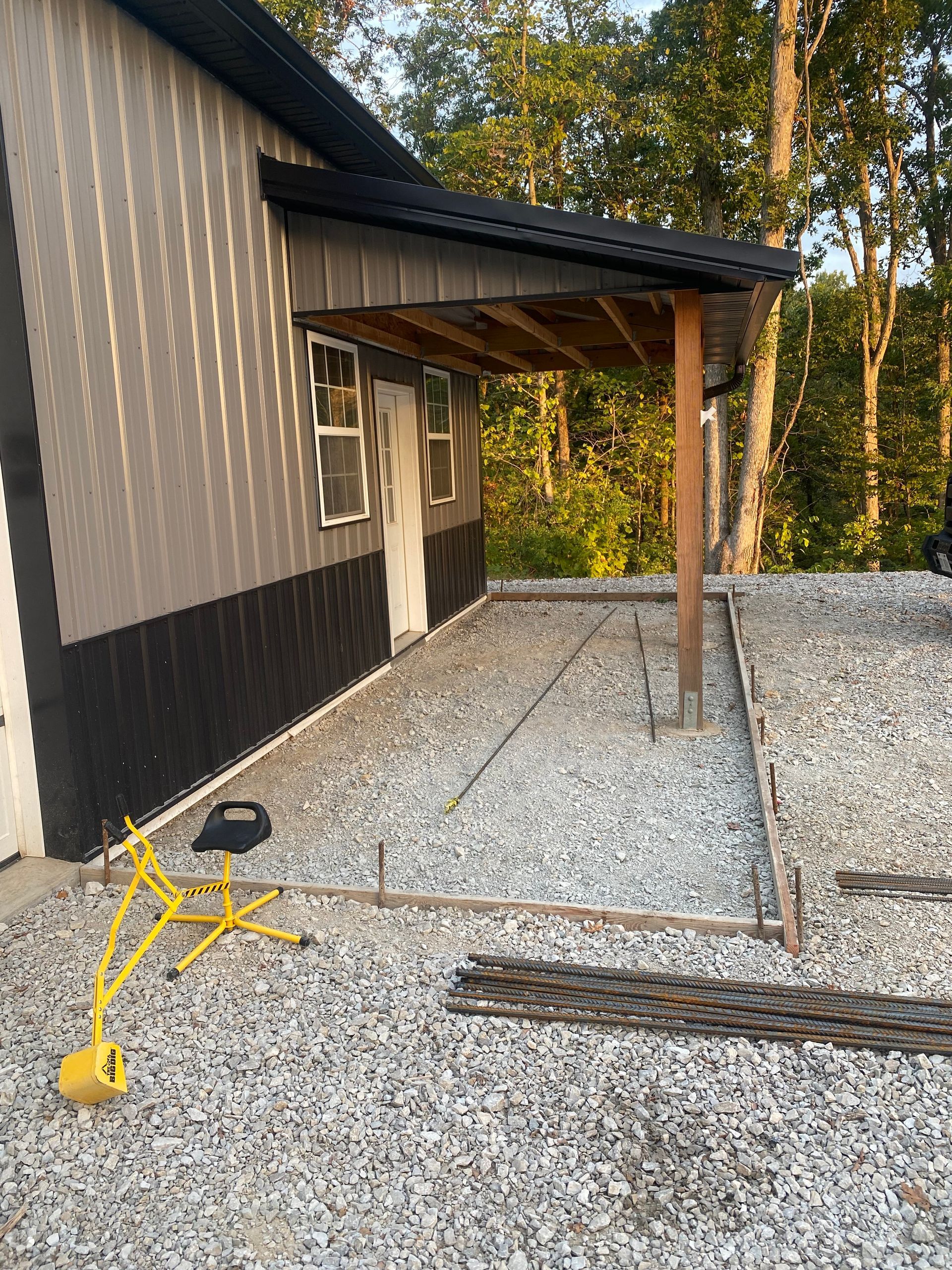 A house with a covered porch is being built on a gravel lot.