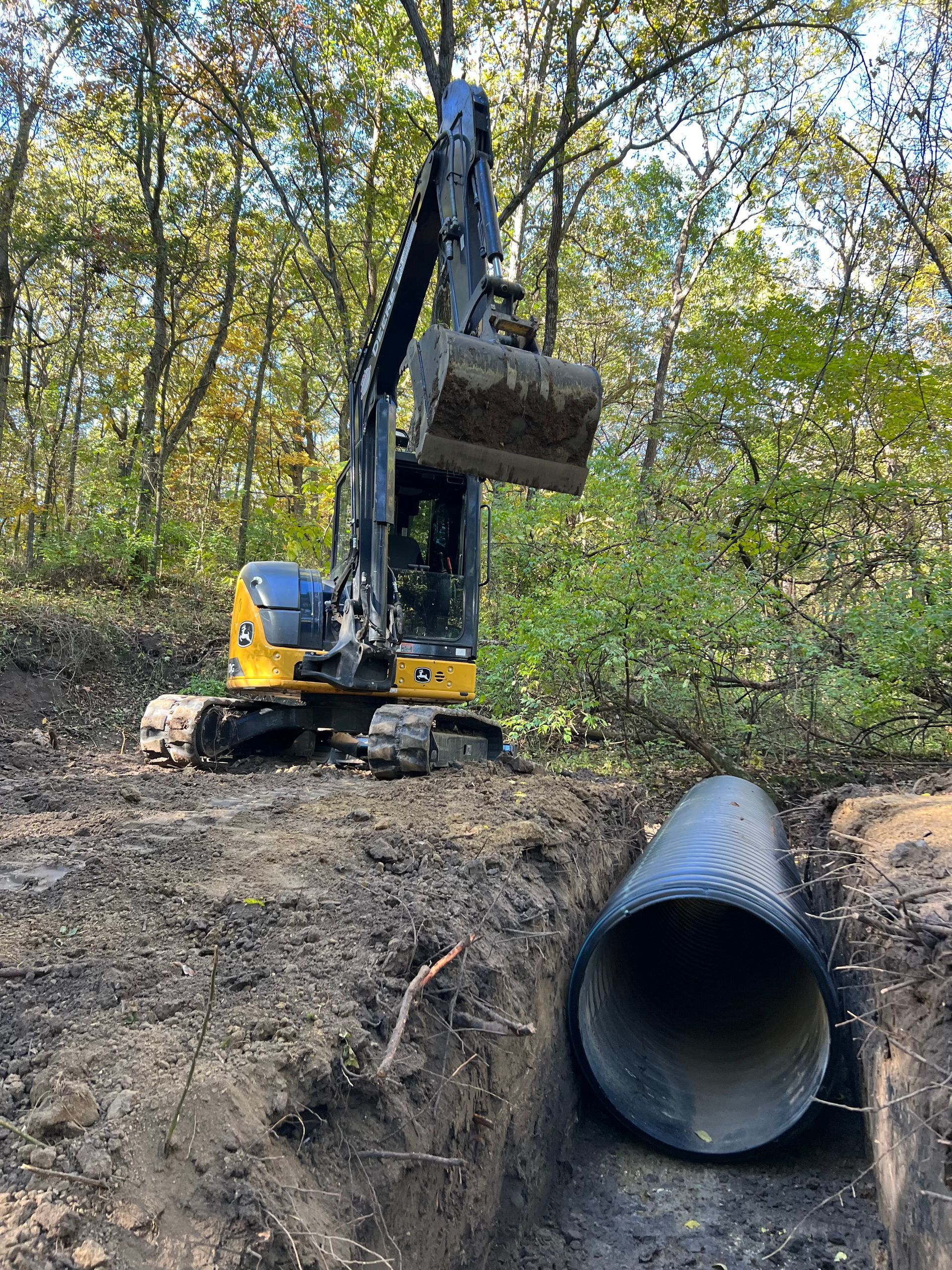 a yellow and black excavator is digging a hole in the ground next to a large pipe .