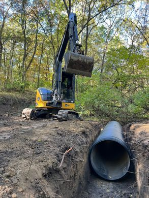 a yellow and black excavator is digging a hole in the ground next to a large pipe .