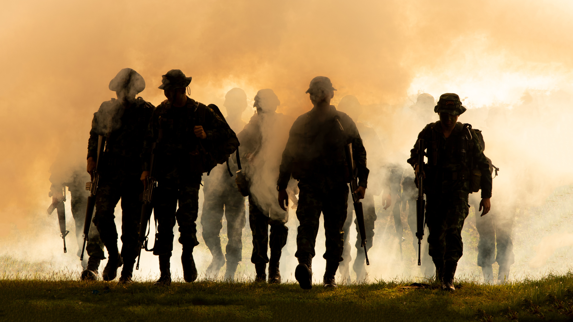 A group of soldiers are walking through smoke in a field.