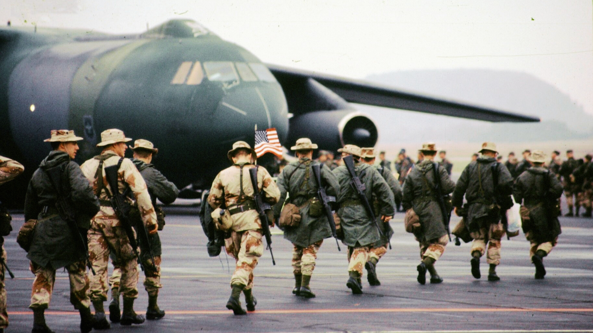 A group of soldiers are standing in a field behind barbed wire fence.
