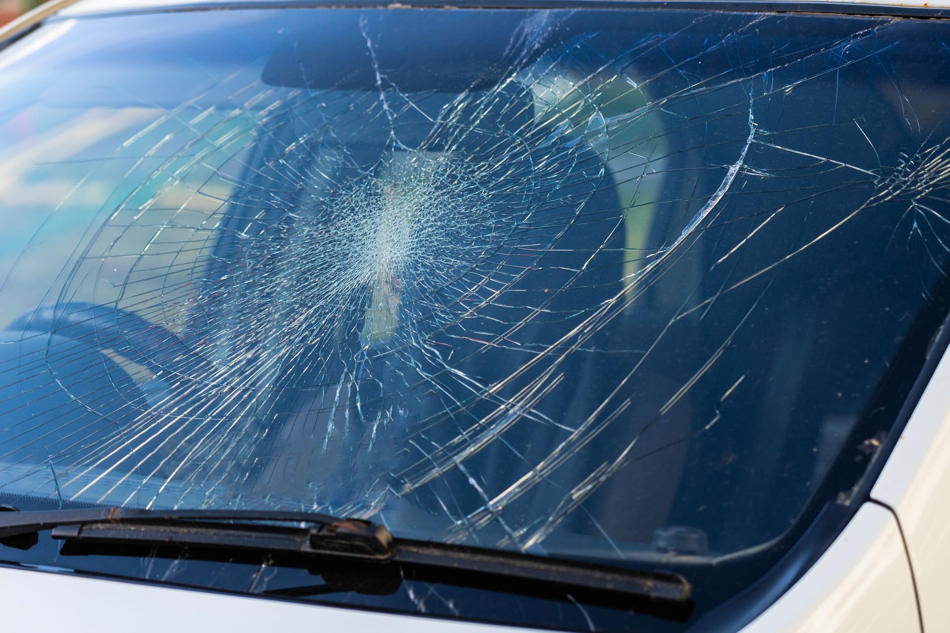 Two auto repair technicians using blue suction cups to lift a car windshield in a garage.