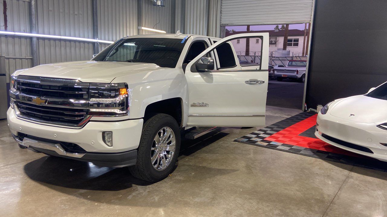 White Chevy pickup truck with open door next to a white Tesla inside a garage.