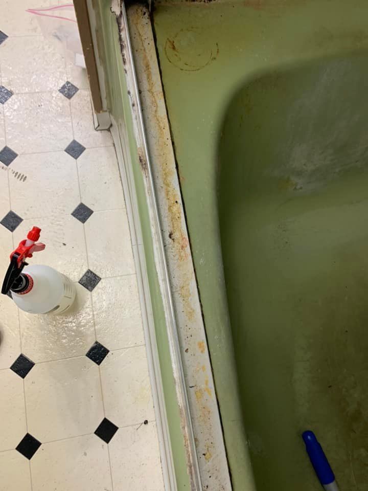 A spray bottle is sitting on the floor next to a bathtub.