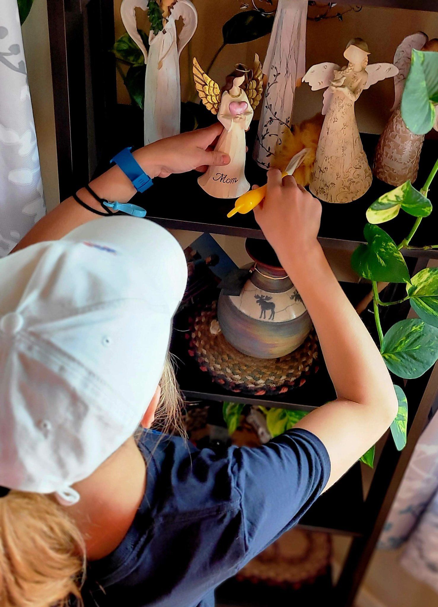 A young girl is painting an angel figurine on a shelf.